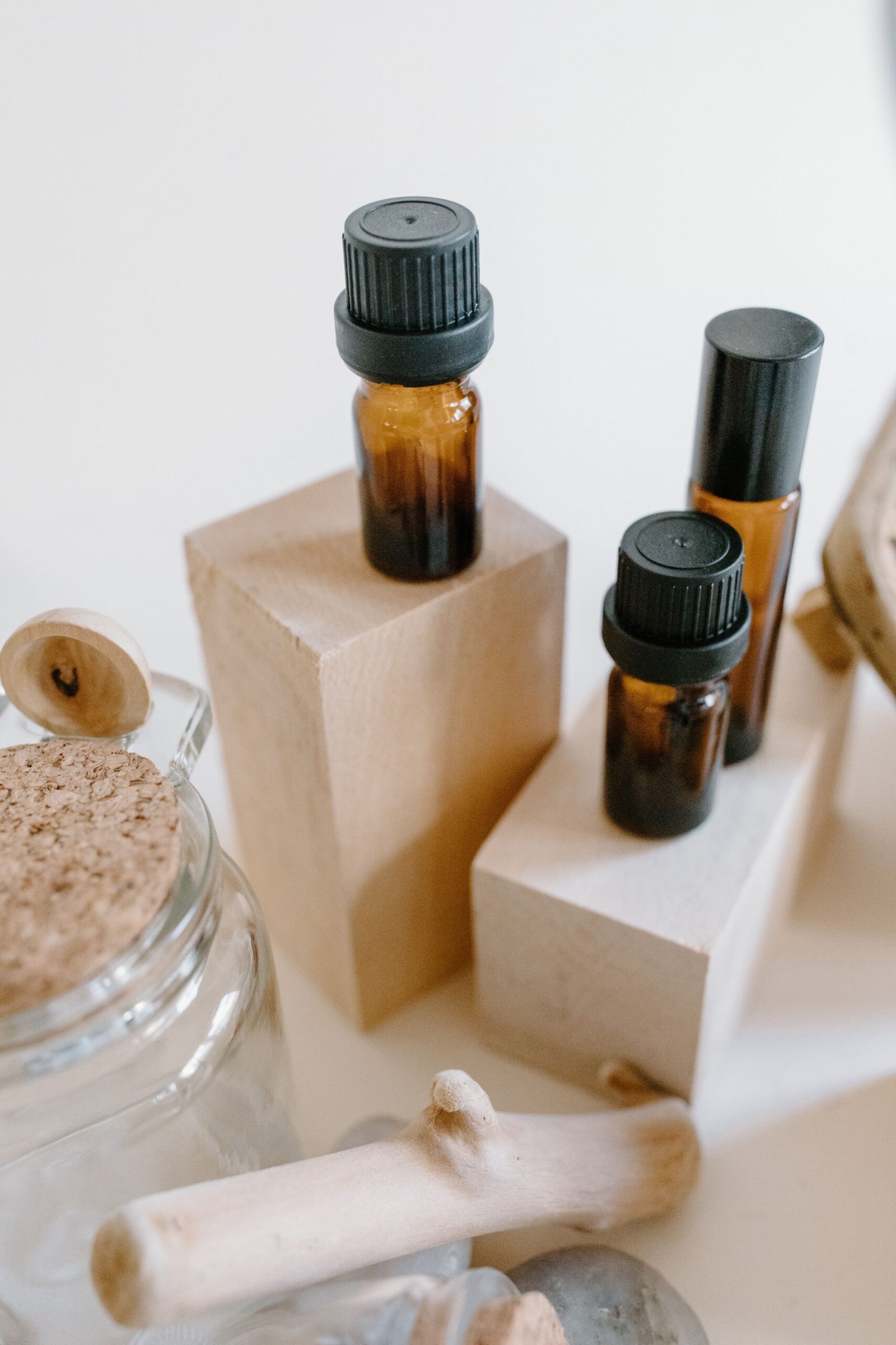 Small amber essential oil bottles with black caps displayed on wooden blocks alongside natural wooden and glass accessories.